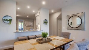 A modern dining area with a wooden table, cushioned chairs, and a central plant. - Ocean-View Home Blocks to Beach with Private Hot Tub & Rooftop Deck! (San Diego)
