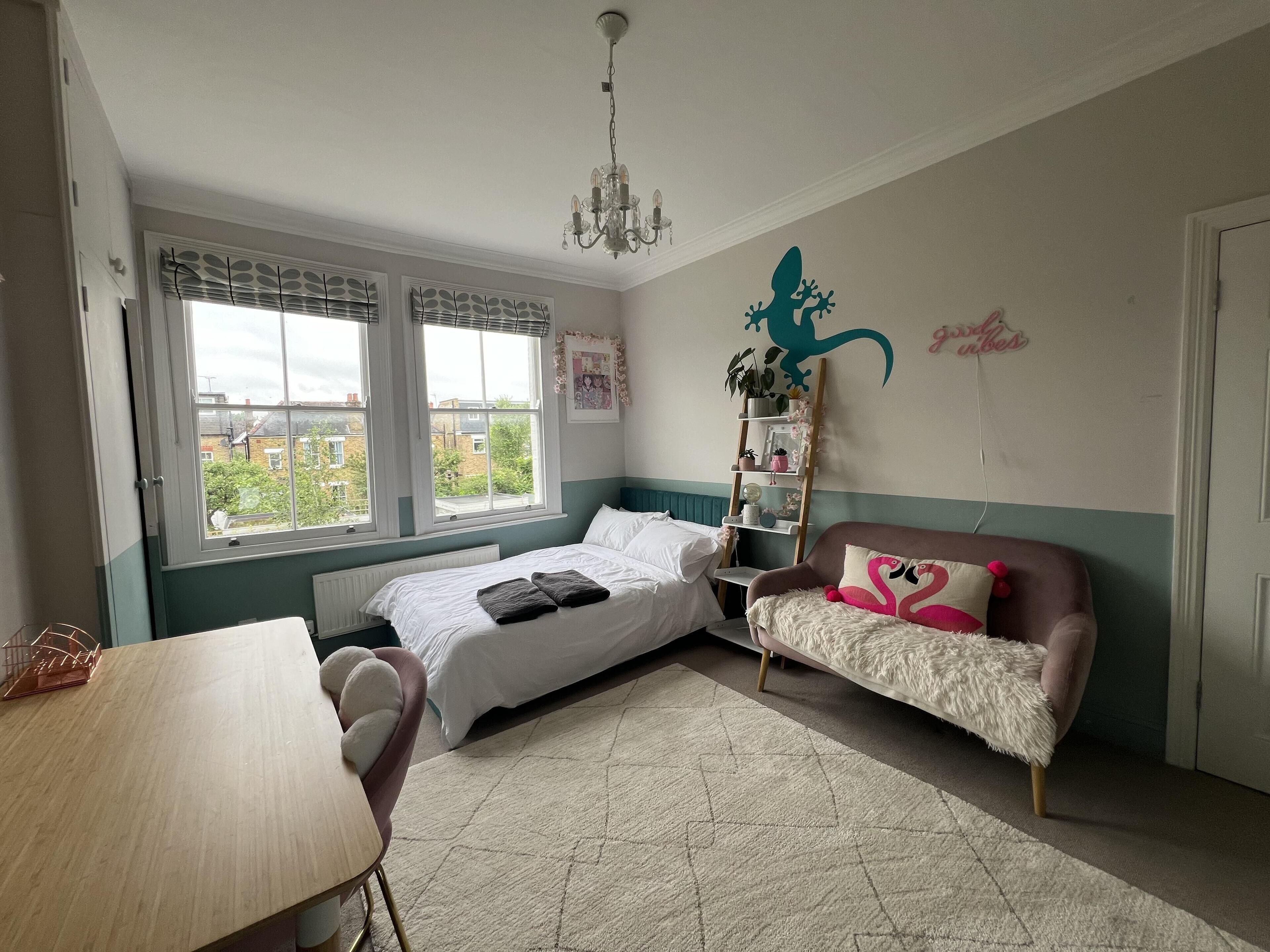 Un dormitorio con cama, escritorio, silla, sofá, candelabro y ventana con vista a edificios.