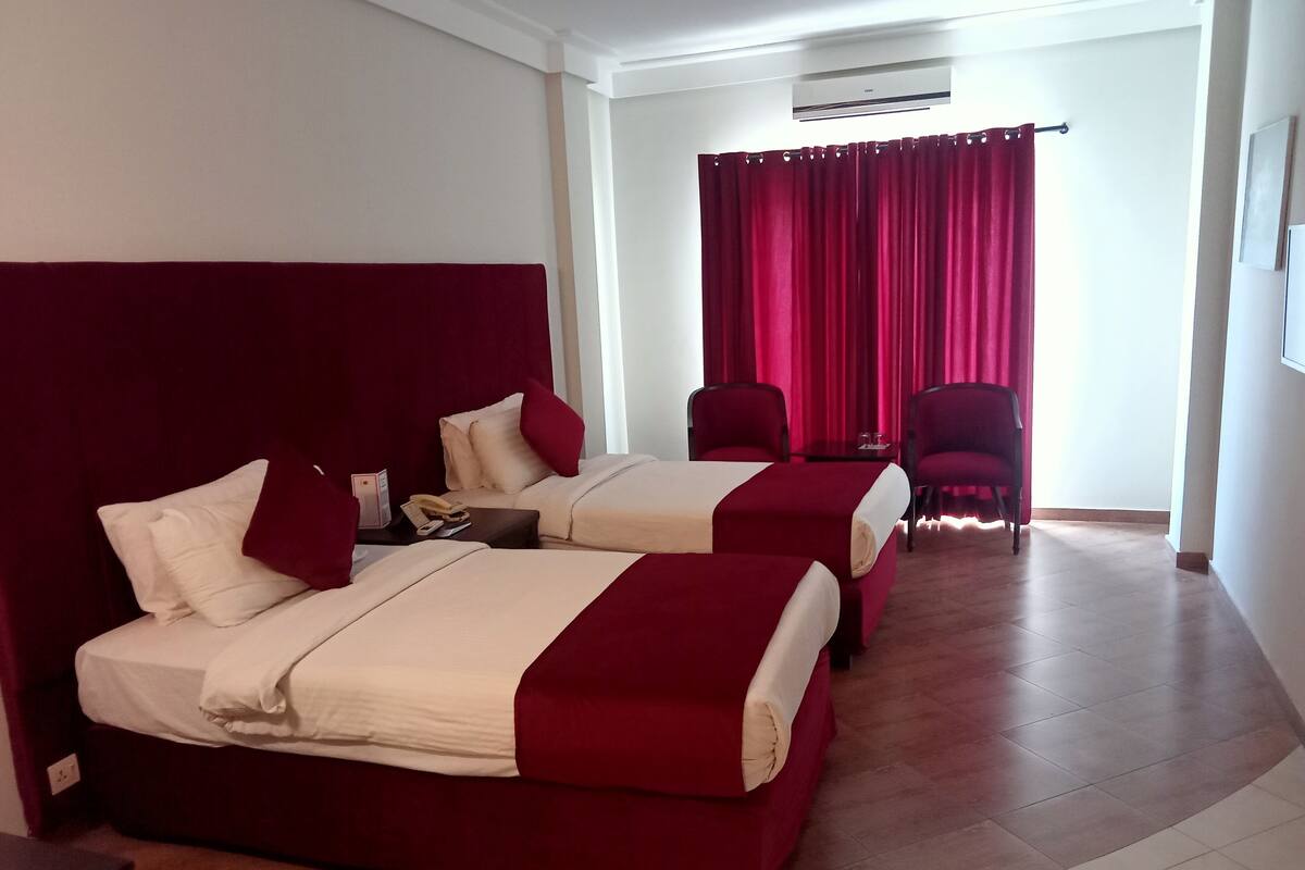 Une chambre d’hôtel avec deux lits, un bureau, une chaise et une fenêtre avec des rideaux rouges.