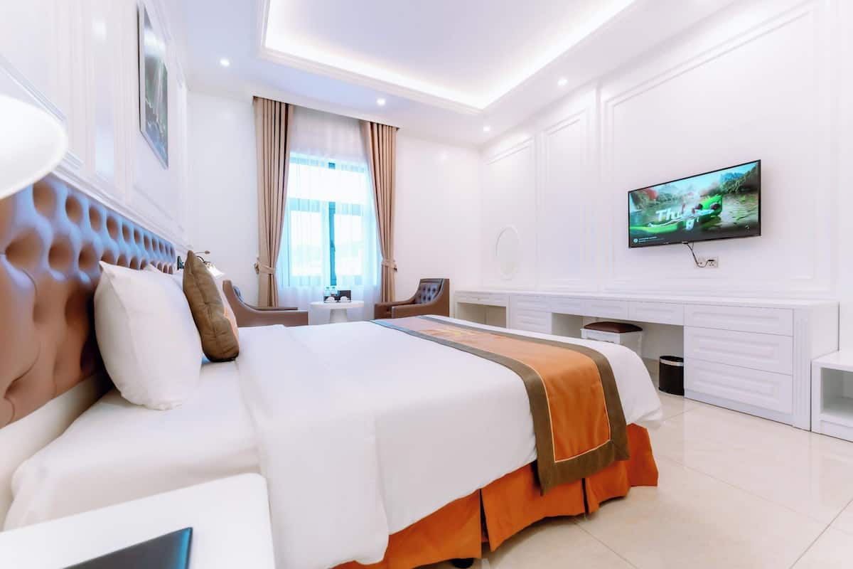 Ein modernes Hotelzimmer mit einem großen Bett, einem an der Wand montierten Fernseher und einem Schreibtisch mit Stuhl.