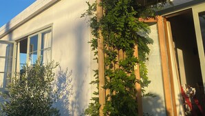 Una casa con una pérgola de madera cubierta de hiedra verde, una terraza de madera y un cielo azul despejado.