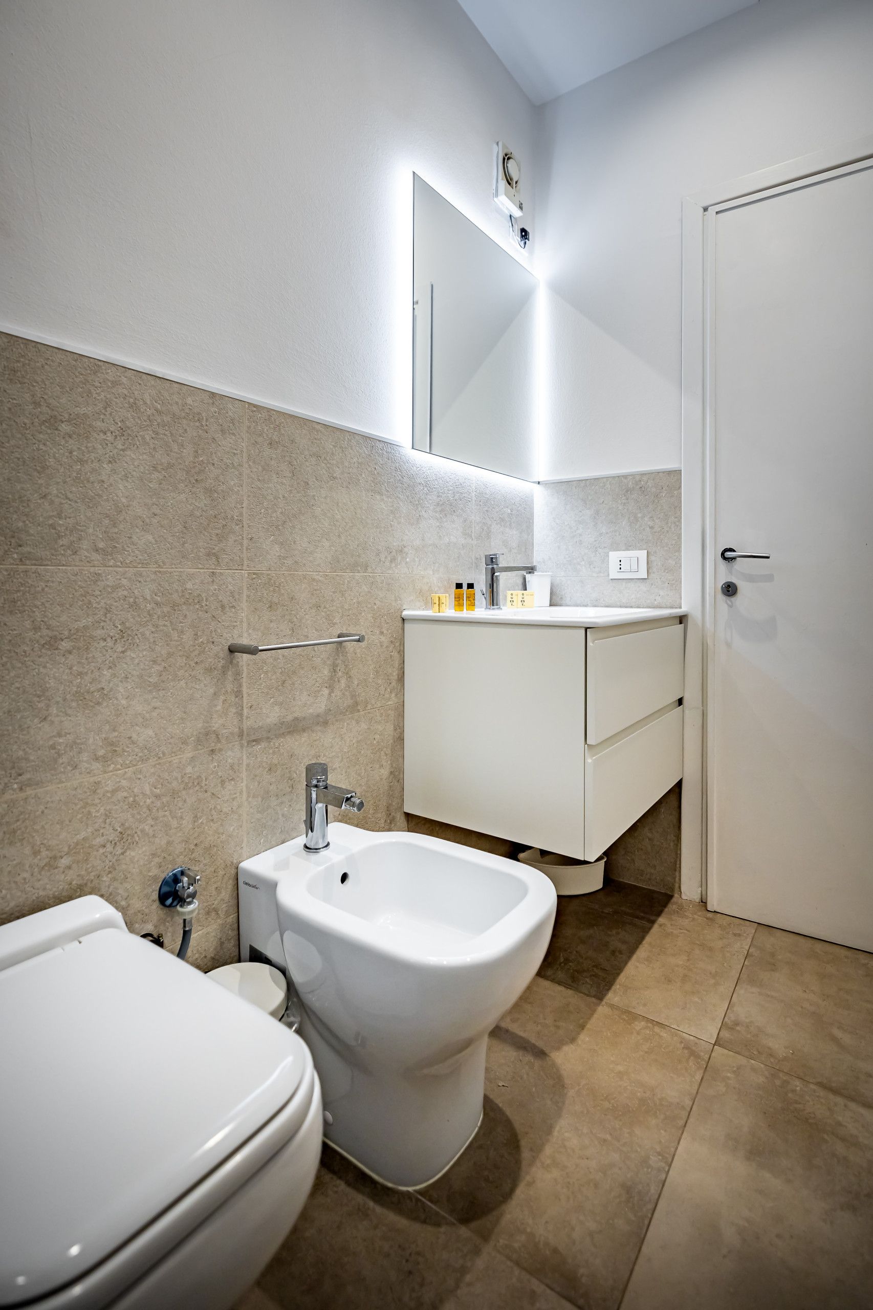 A modern bathroom with a bidet, toilet, and a vanity with a mirror.