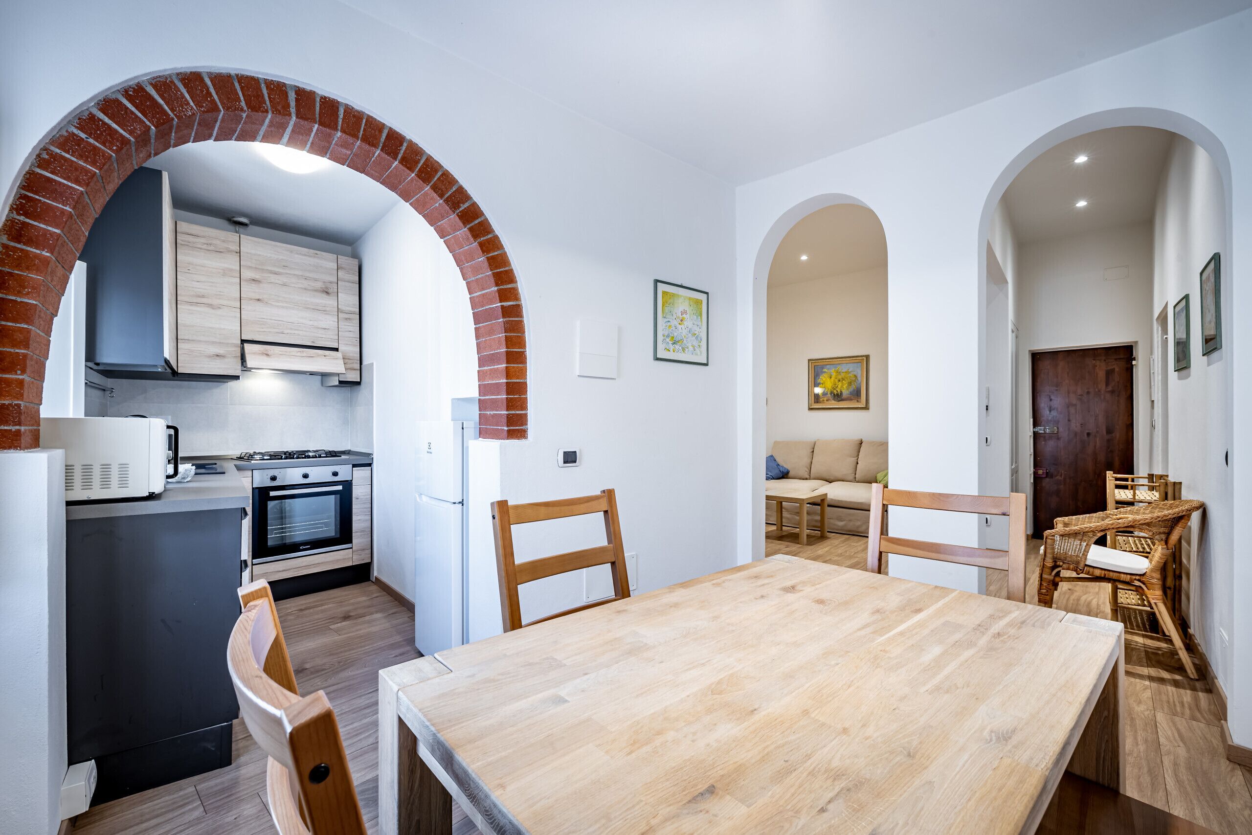 Een moderne keuken met een boogvormige doorgang, een eethoek met een houten tafel en stoelen, en een woonkamer met een bank en een schilderij.