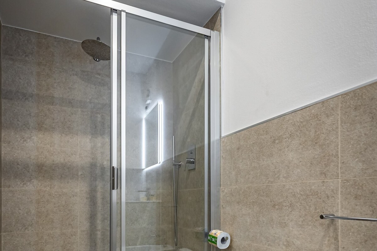 A modern bathroom with a glass-enclosed shower, a toilet, and a bidet.