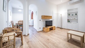 A modern living room with a TV, wooden entertainment unit, a dining area, and a white shelving unit. - YiD Pilastri (Florence)