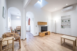 Un salon moderne comprenant un téléviseur, un meuble de rangement en bois, un coin repas et une étagère blanche.