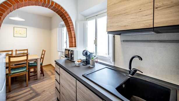 Una cocina moderna con un arco de ladrillo, armarios de madera, un lavamanos negro y un comedor con mesa y sillas.