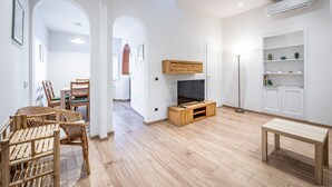 Una sala moderna con una unidad de entretenimiento de madera, un televisor, un comedor con sillas y un estante blanco.