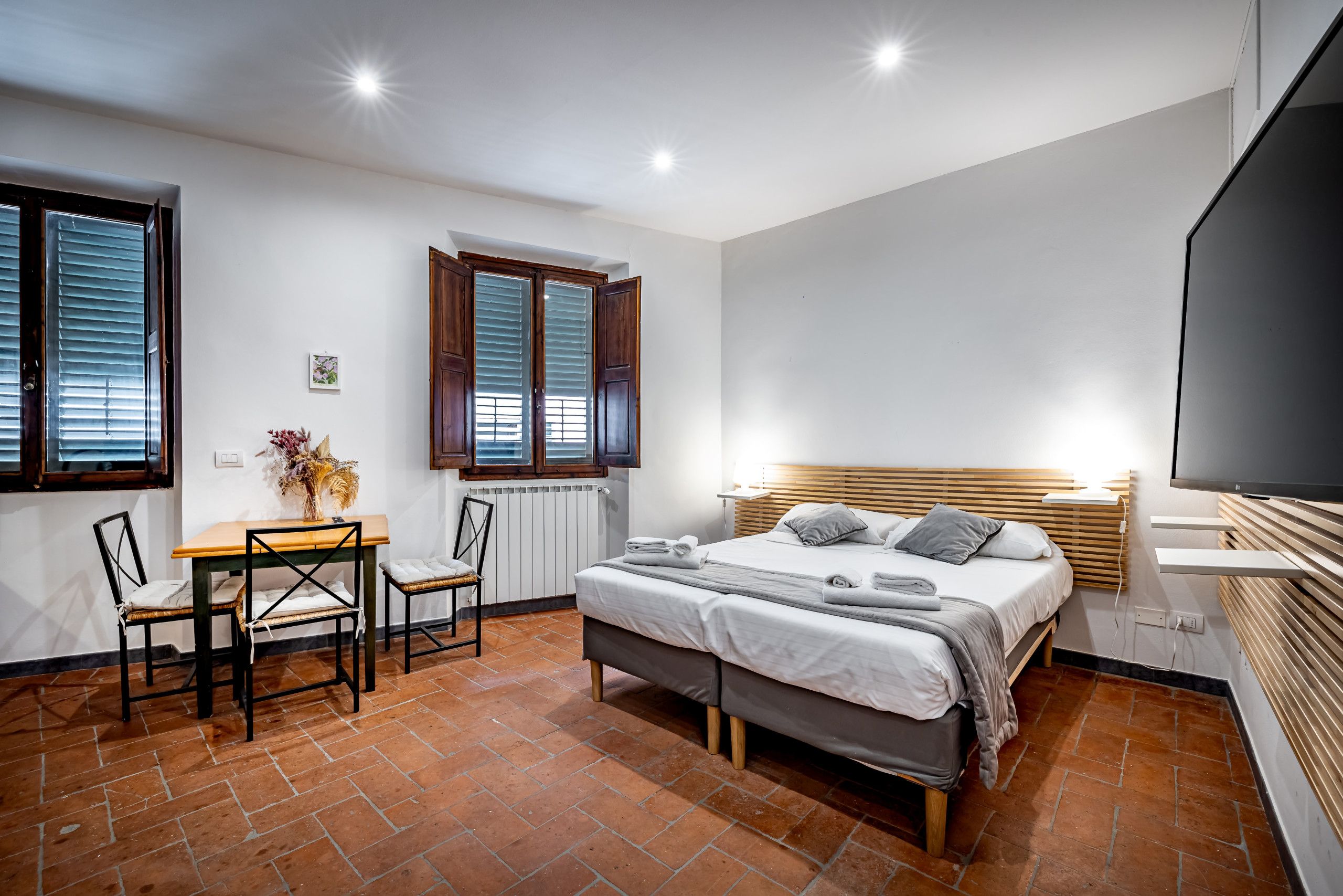 A bedroom with a bed, bedside table, chair, and a TV.