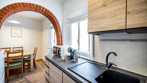 A kitchen with a brick archway, wooden cabinets, a black sink, and a dining area with chairs and a table. - YiD Pilastri (Florence)