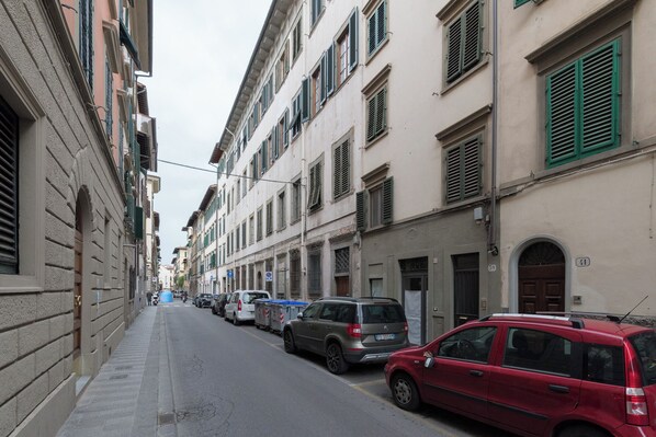 A narrow street lined with multi-story buildings, parked cars, and a sidewalk. - YiD Pilastri (Florence)