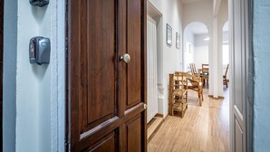 Un pasillo con puerta de madera, un portero automático en la pared y un comedor con sillas y una mesa.