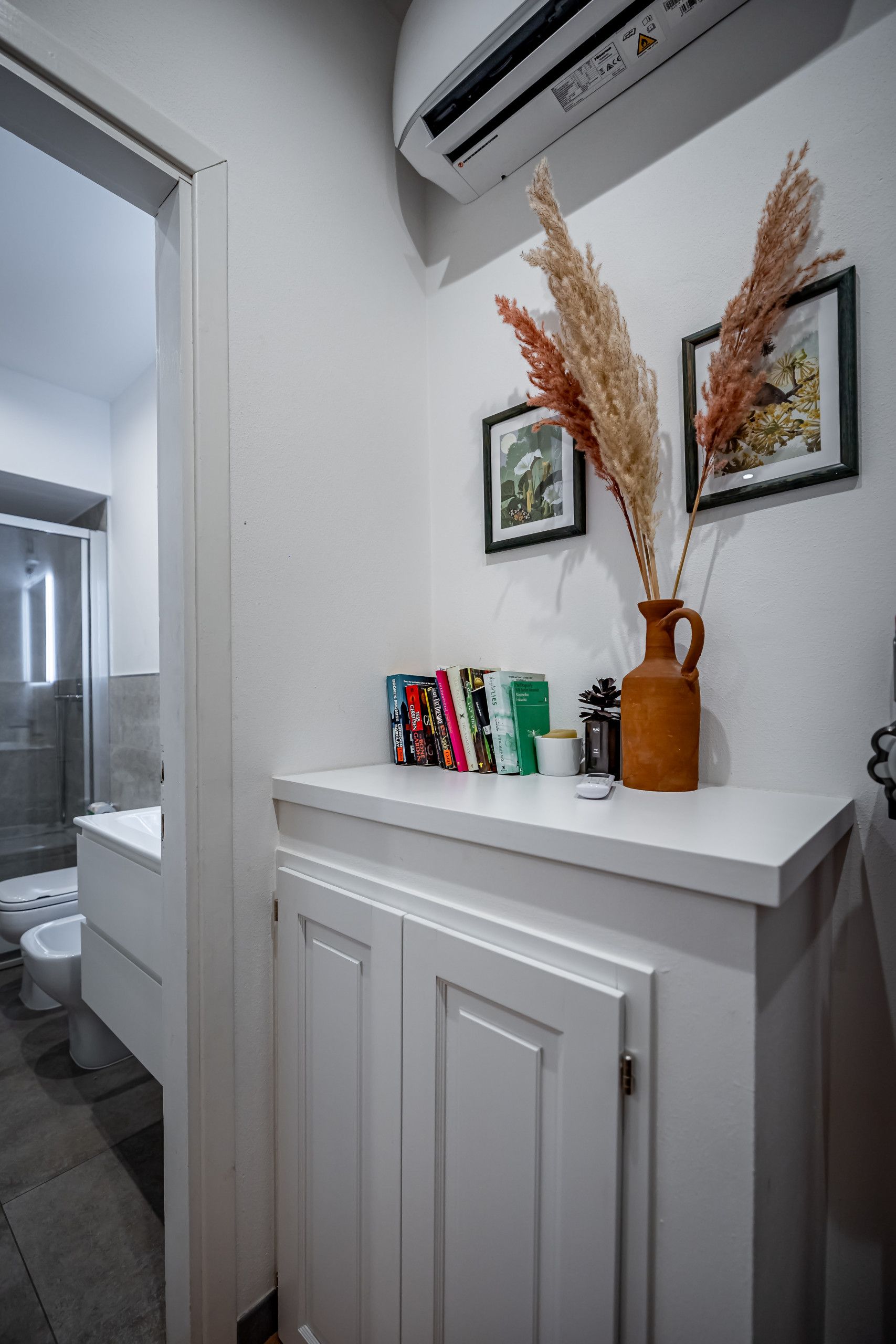Une salle de bain avec un meuble-lavabo blanc, une douche et un climatiseur fixé au mur.