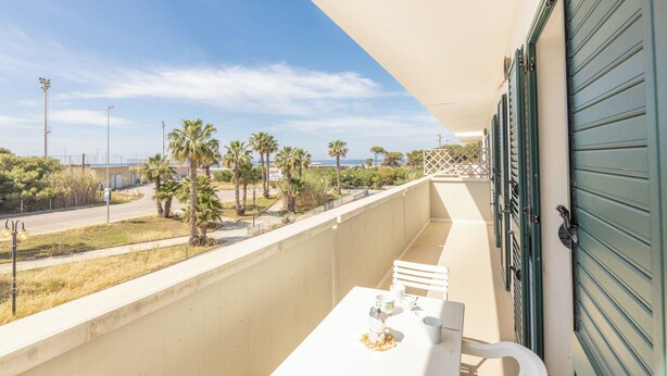 A balcony with a table and chairs, overlooking a street with palm trees and a clear sky. - Apartment Balcony Sea View - Gallipoli (Gallipoli)