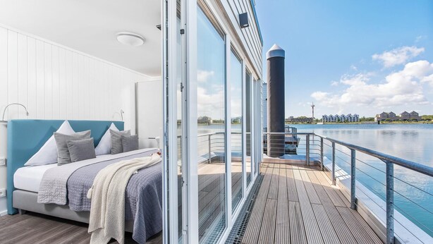 Quarto moderno com uma cama grande, vista para a água e varanda com guarda-corpo.