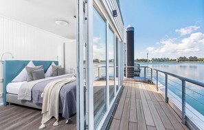 Une chambre moderne avec un grand lit, une vue sur l’eau et un balcon doté d’une balustrade.