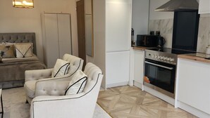 Une cuisine moderne dotée d’un four et d’un micro-ondes encastrés, un coin repas avec un canapé et des chaises, et un salon séparé avec un lit à tête de lit capitonnée.