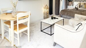 Une chambre d’hôtel moderne dotée d’un coin repas, d’un canapé, d’un lit et d’un grand téléviseur fixé au mur, qui diffuse une scène de coucher de soleil.