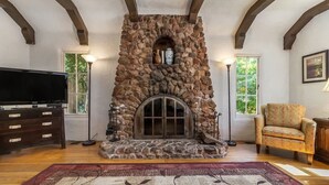 A stone fireplace with a television on a wooden cabinet, a patterned rug, and a chair.