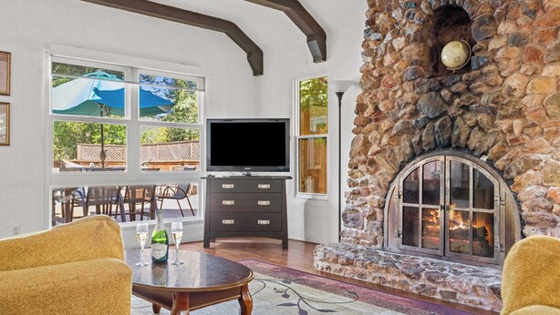 A stone fireplace, a television, and a dining area with outdoor views.