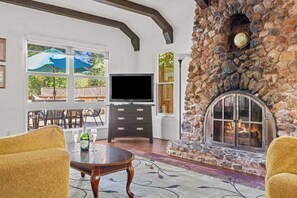 A stone fireplace, a television, and a dining area with outdoor views.