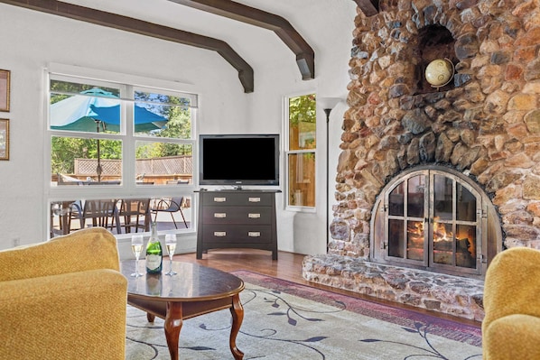 A stone fireplace, a television, and a dining area with outdoor views.