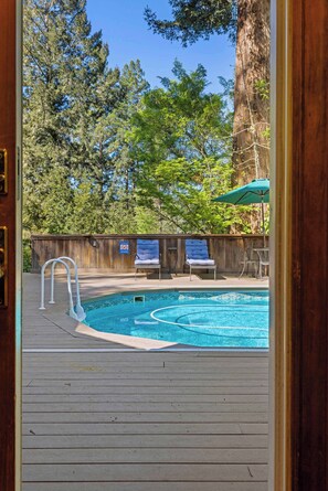 Una terraza de madera con piscina, dos sillones de descanso y un gran árbol.