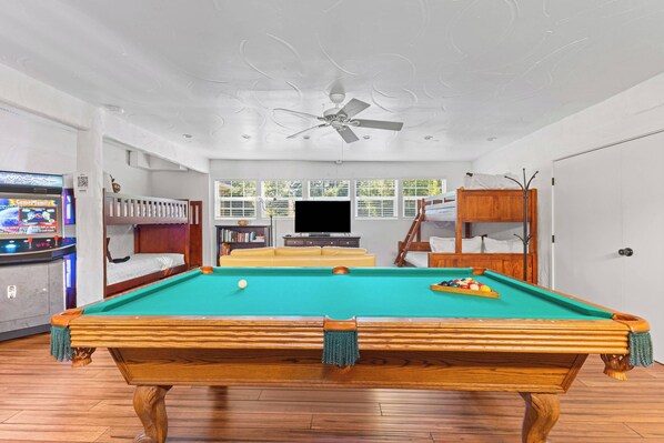 A pool table in a room with a ceiling fan, a television, and a window with blinds.