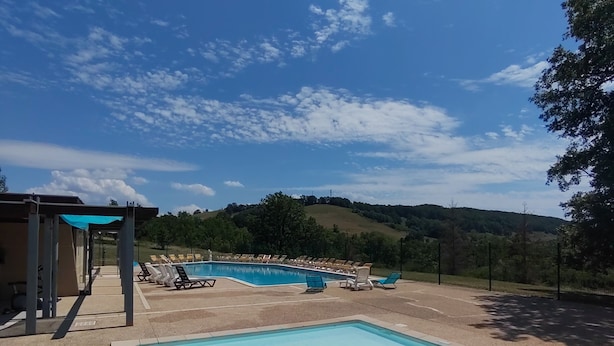 Une piscine dotée de chaises longues et d’un espace abrité, le tout entouré d’un paysage vallonné.