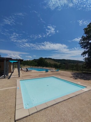 A swimming pool with lounge chairs and a covered area, surrounded by a hilly landscape. - Cottage in holiday village (Caylus)