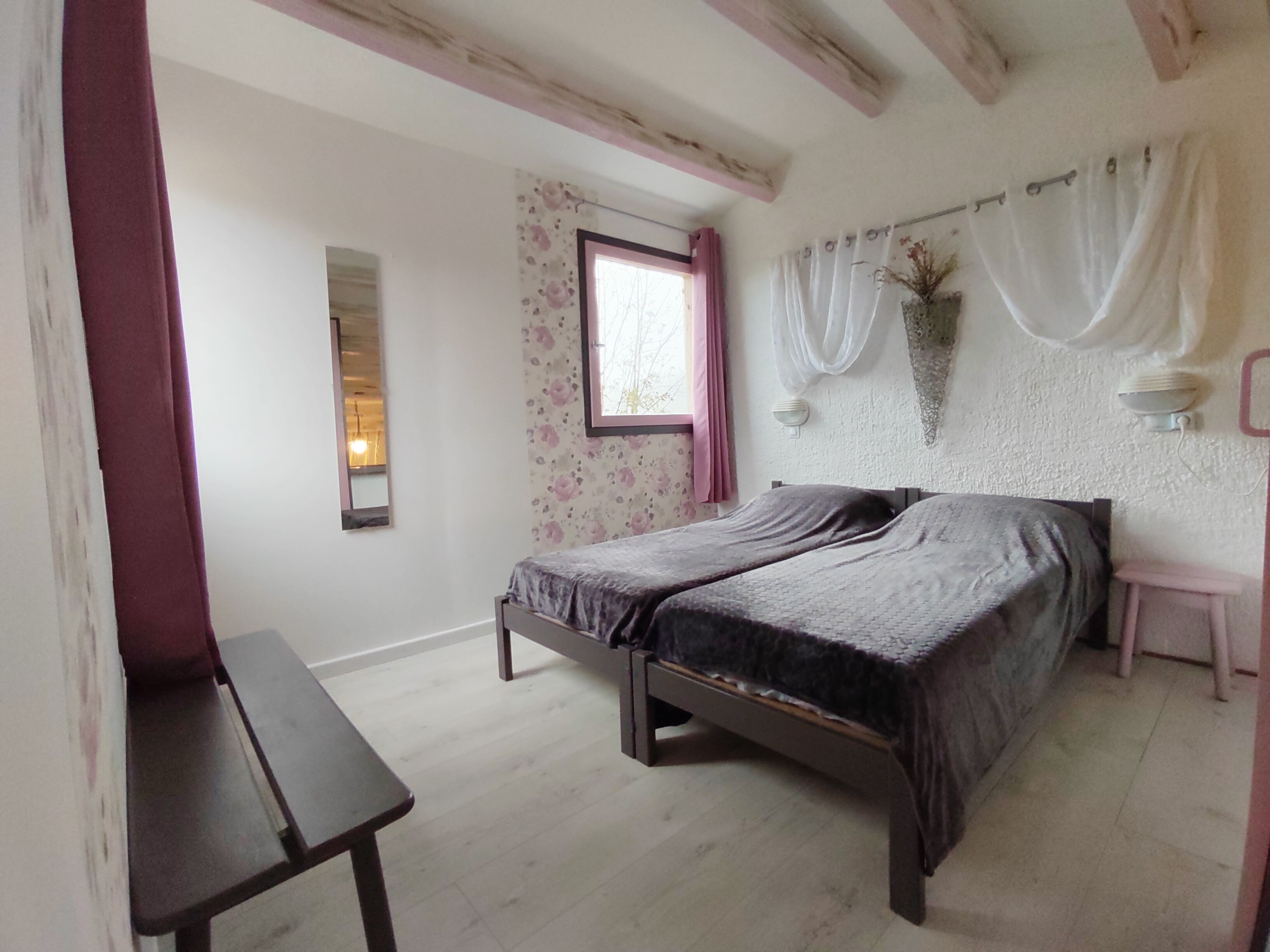 A bedroom with a bed, a bedside table, a window with curtains, and a wall-mounted mirror.