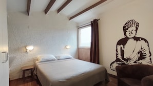 Une chambre à coucher avec un lit, des tables de chevet, une fresque représentant un Bouddha accrochée au mur et une fenêtre avec des rideaux.