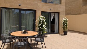 An outdoor patio with a round wooden table and chairs, surrounded by potted plants and a glass door leading to a balcony. - ASTER sea & spa dúplex (Villajoyosa)