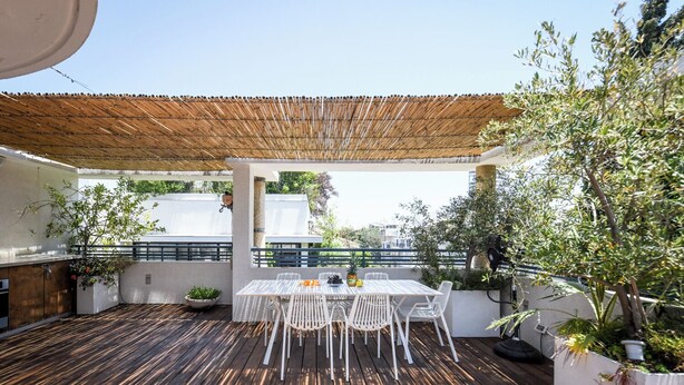 An outdoor patio with a wooden deck, white chairs, a table, and a pergola. - Spacious 3BR Penthouse w Rooftop (Tel Aviv)