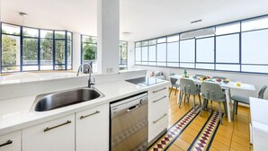 A modern kitchen with a dishwasher, sink, and dining area with chairs and a table. - Spacious 3BR Penthouse w Rooftop (Tel Aviv)