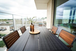 A balcony with a wooden table, chairs, a vase with branches, and wine glasses. - BE OST Vict 25-0202 in Oostende (Ostend)