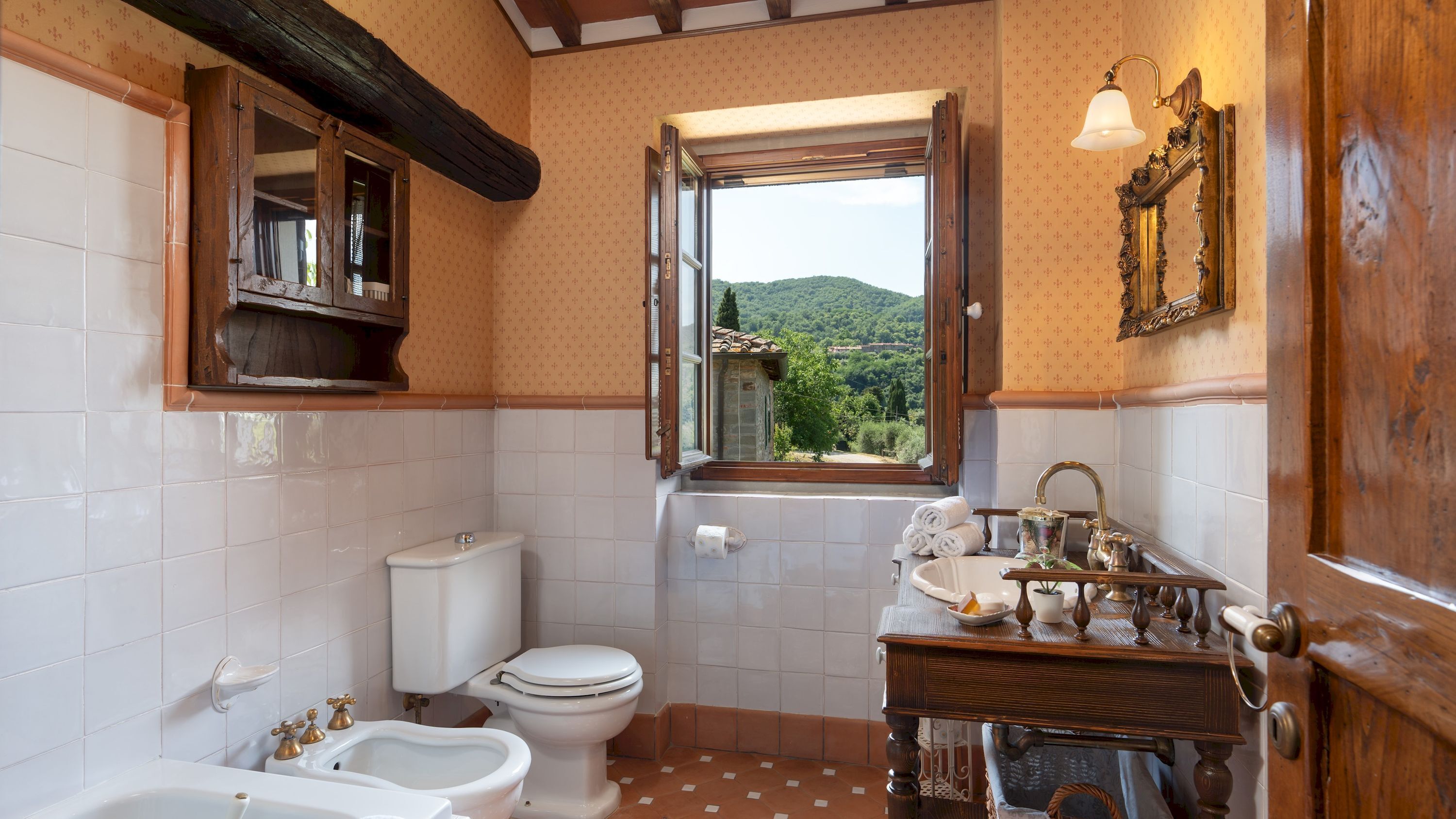 Een badkamer met toilet, bidet, wastafel en een raam met uitzicht op het landschap.