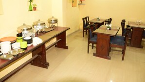 A dining area with a long wooden table, several chairs, and a buffet setup with various dishes and containers. - Hotel Ayaan Residency Manali  (Manali)