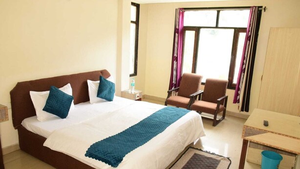 A hotel room with a large bed, two chairs, a small table, and a window with curtains. - Hotel Ayaan Residency Manali  (Manali)
