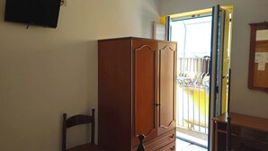 Une pièce comprenant une armoire en bois, une chaise, une petite table et un téléviseur fixé au mur.
