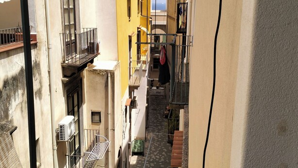Une ruelle étroite, bordée d’immeubles dotés de balcons, d’où l’on a une vue dégagée sur le ciel.