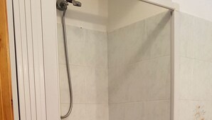 Een inloopdouche met een glazen deur, witte betegelde wanden en een houten deurkozijn.