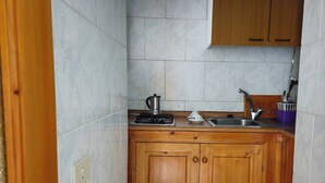 Een compacte keuken met houten kastjes, een gasfornuis, een spoelbak en een koffiezetapparaat.