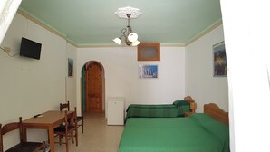 Een kamer met een houten deur, een kleine tafel met stoelen, een bed met groene beddengoed, een plafondventilator en een tv aan de muur.
