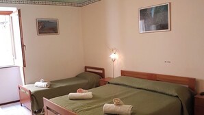 Une chambre avec deux lits simples, un bureau en bois, une chaise, une lampe et un ventilateur de plafond.