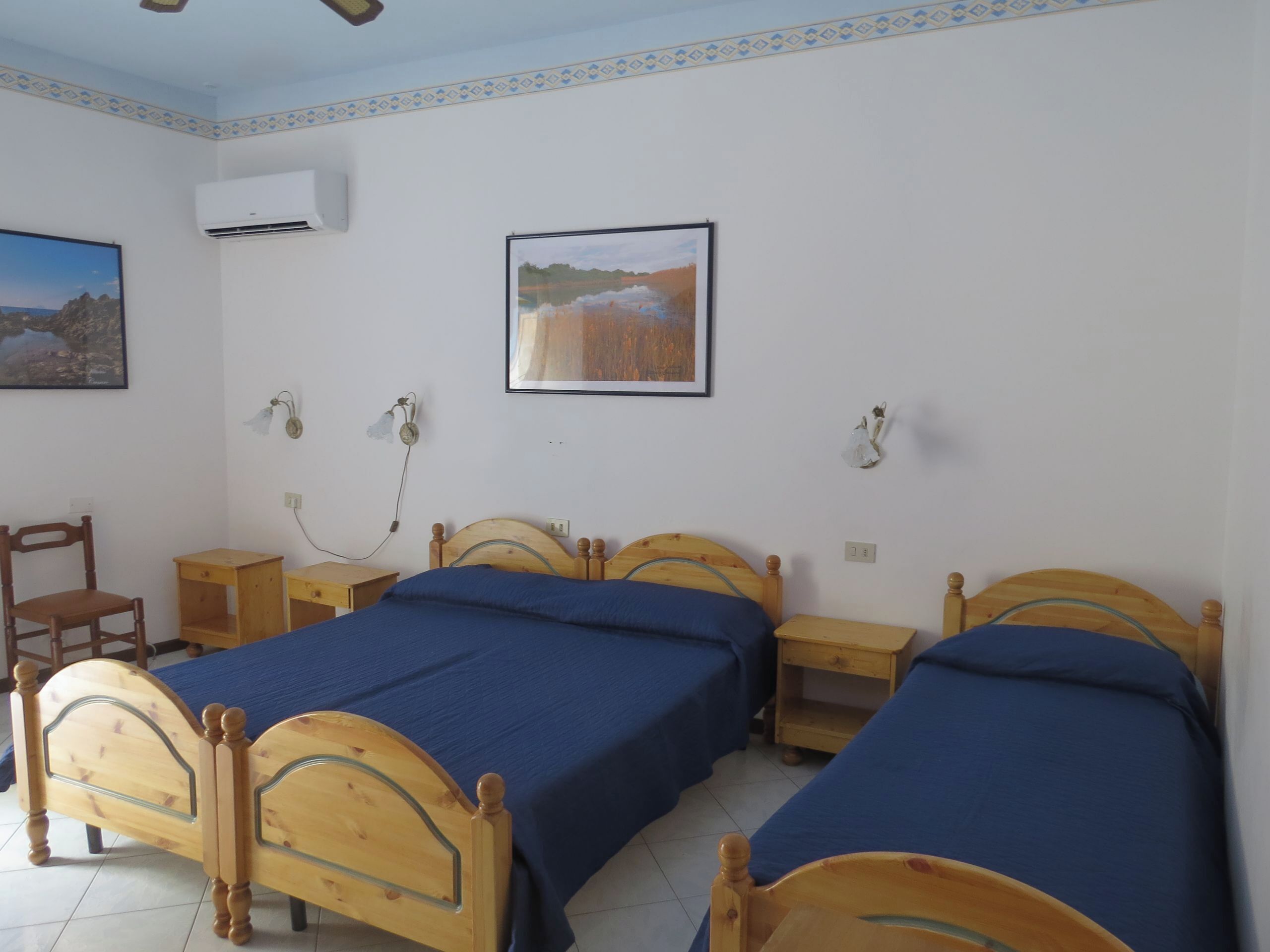 Ein Zimmer mit zwei Holzbetten, einem Sessel, einem kleinen Tisch und zwei Wandlampen.