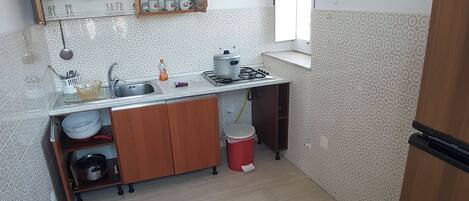 Een koelkast, een kookplaat, kookgerei, borden en bestek, een eettafel