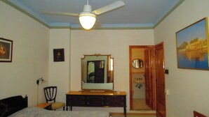 A bedroom with a bed, a dresser, a mirror, a ceiling fan, and a door leading to a bathroom. - single room with ceiling fan (Lipari)