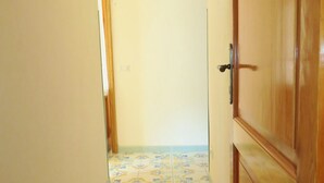A narrow hallway with patterned floor tiles, wooden doors, and a light switch on the wall. - mivigio dual use (Lipari)