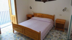A bedroom with a wooden bed, two bedside tables, a wall-mounted fan, and a balcony door. - mivigio dual use (Lipari)